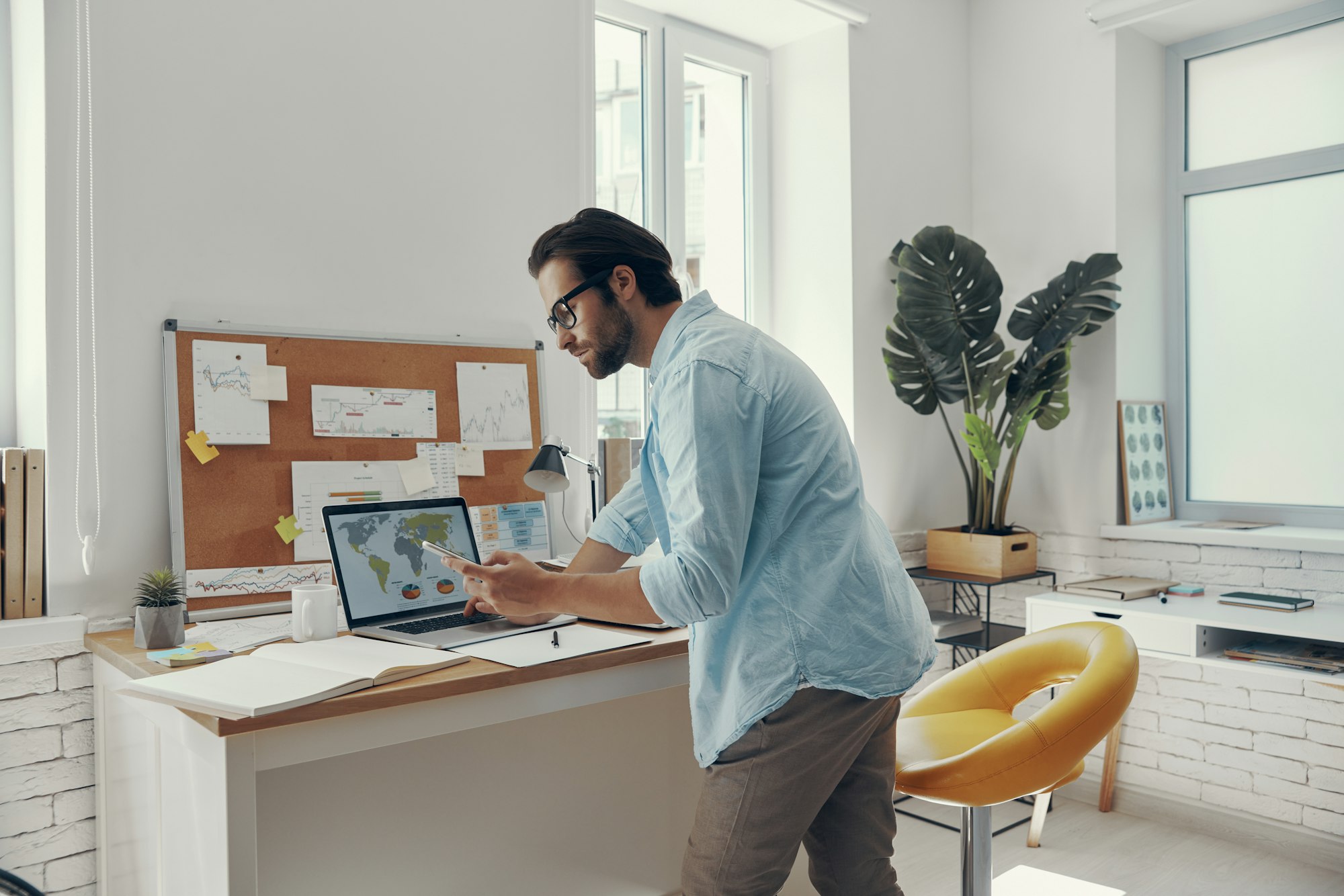 Confident young man looking at laptop while standing near his working place